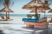 Picture of a pair of glasses on top of a pile of books. Background is a beach with umbrellas